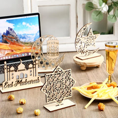 Decorative wooden 'Eid Mubarak' items on a table with food and a laptop in the background.