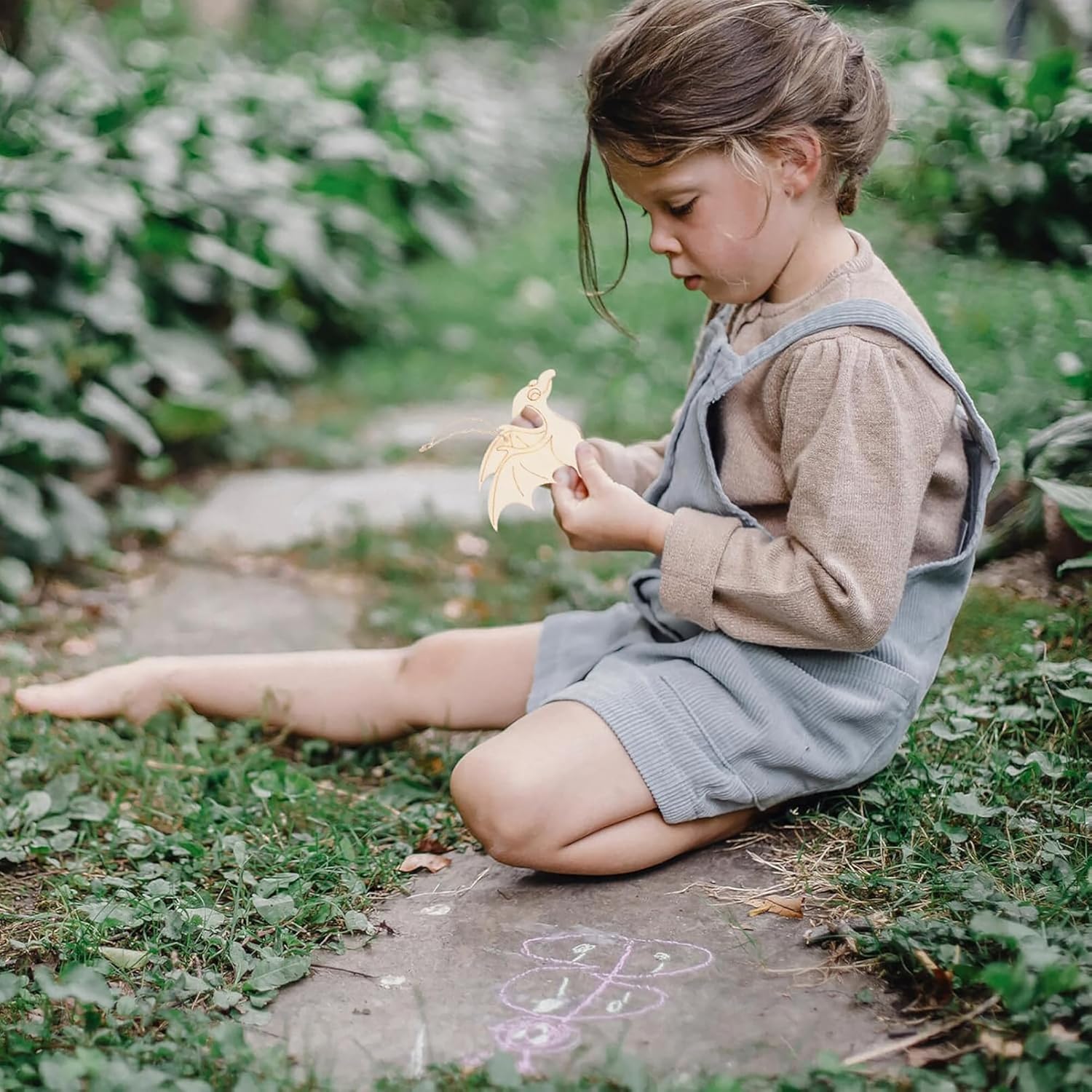 Young girl sitting on grass holding a leaf in a garden