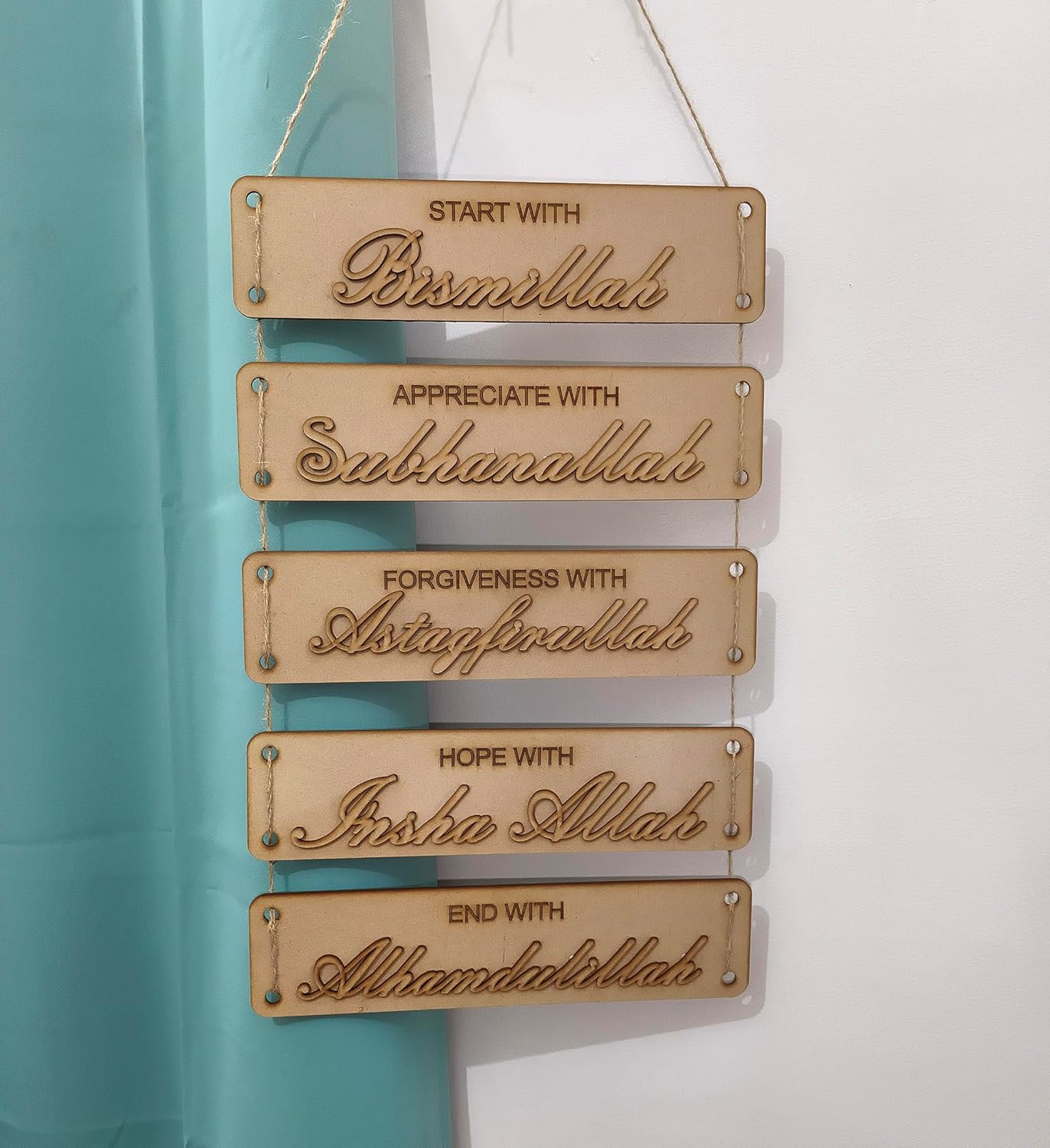 Wooden plaque with engraved Arabic phrases on a light blue and white background