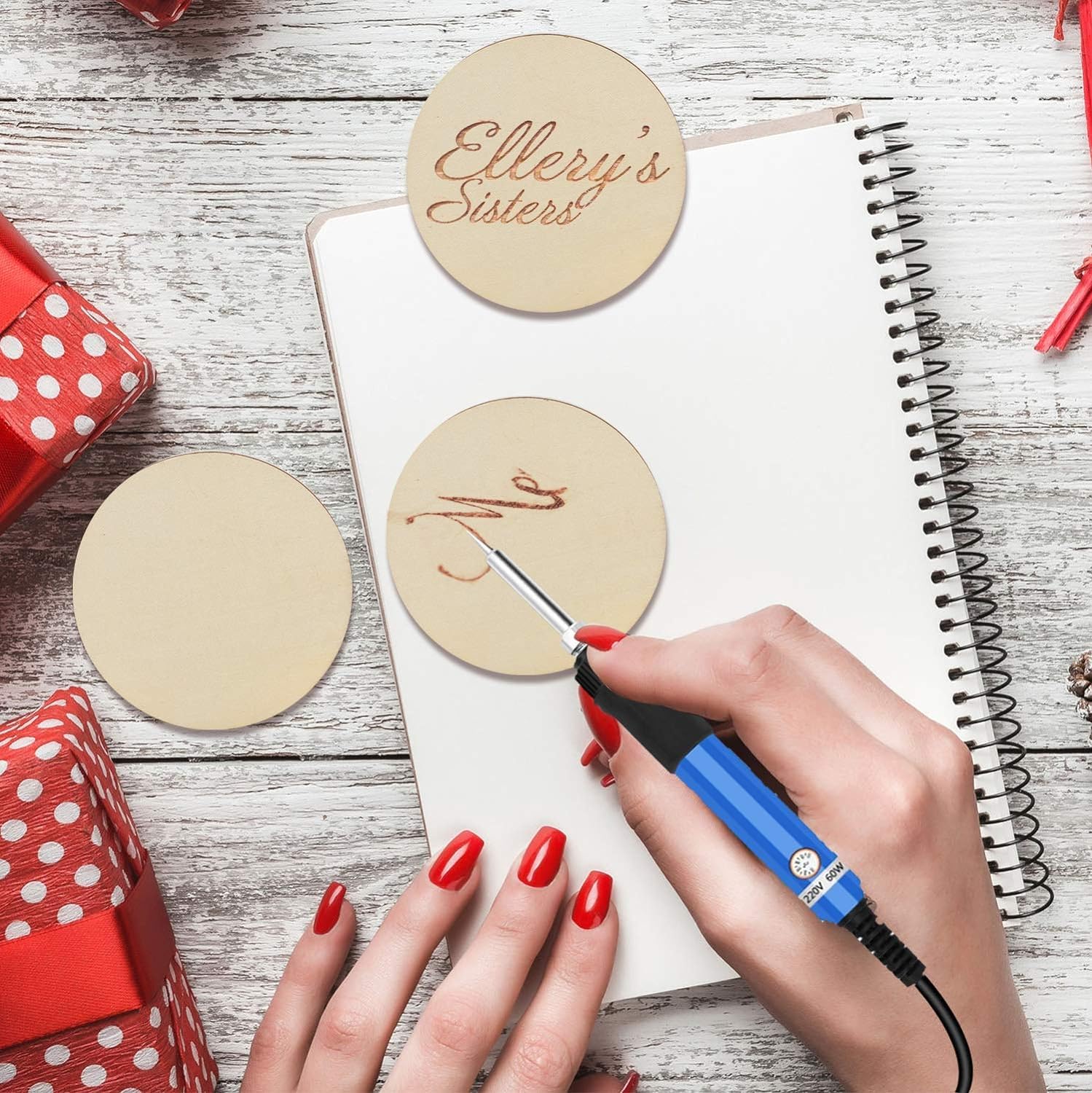 Person using a hot glue gun to attach wooden coasters with engraved text to a notebook on a wooden surface.