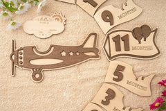 Wooden baby milestone markers with numbers and airplane design on a wooden surface.
