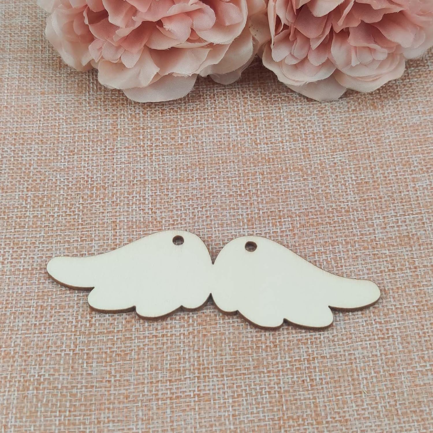 Two wooden angel wing shapes on a textured fabric background with pink flowers.