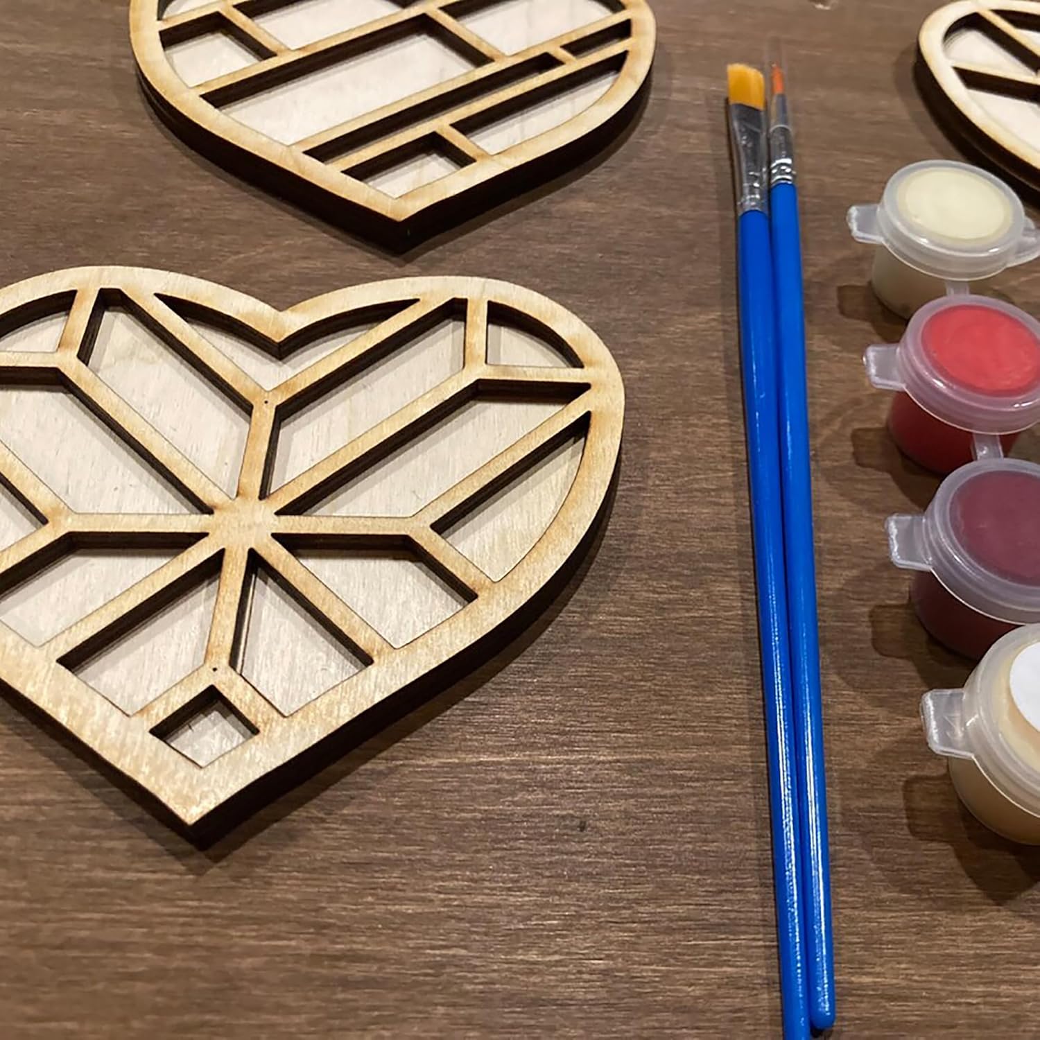 Wooden heart-shaped cutouts with paintbrushes and paint containers on a wooden surface