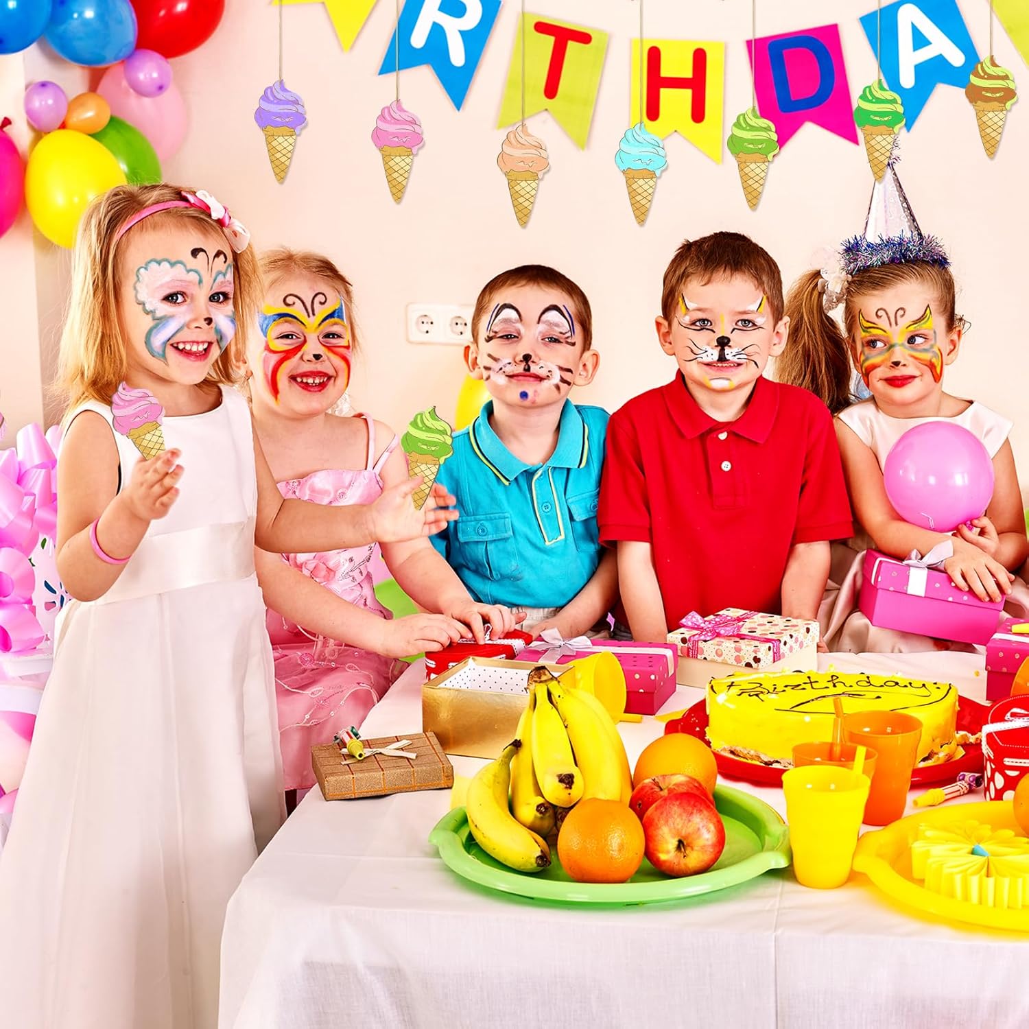 Children with face paint at a birthday party, sitting around a table with cake and balloons.