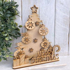 Wooden Christmas tree decoration with ornaments and 'Merry Christmas' text on a light wooden background.