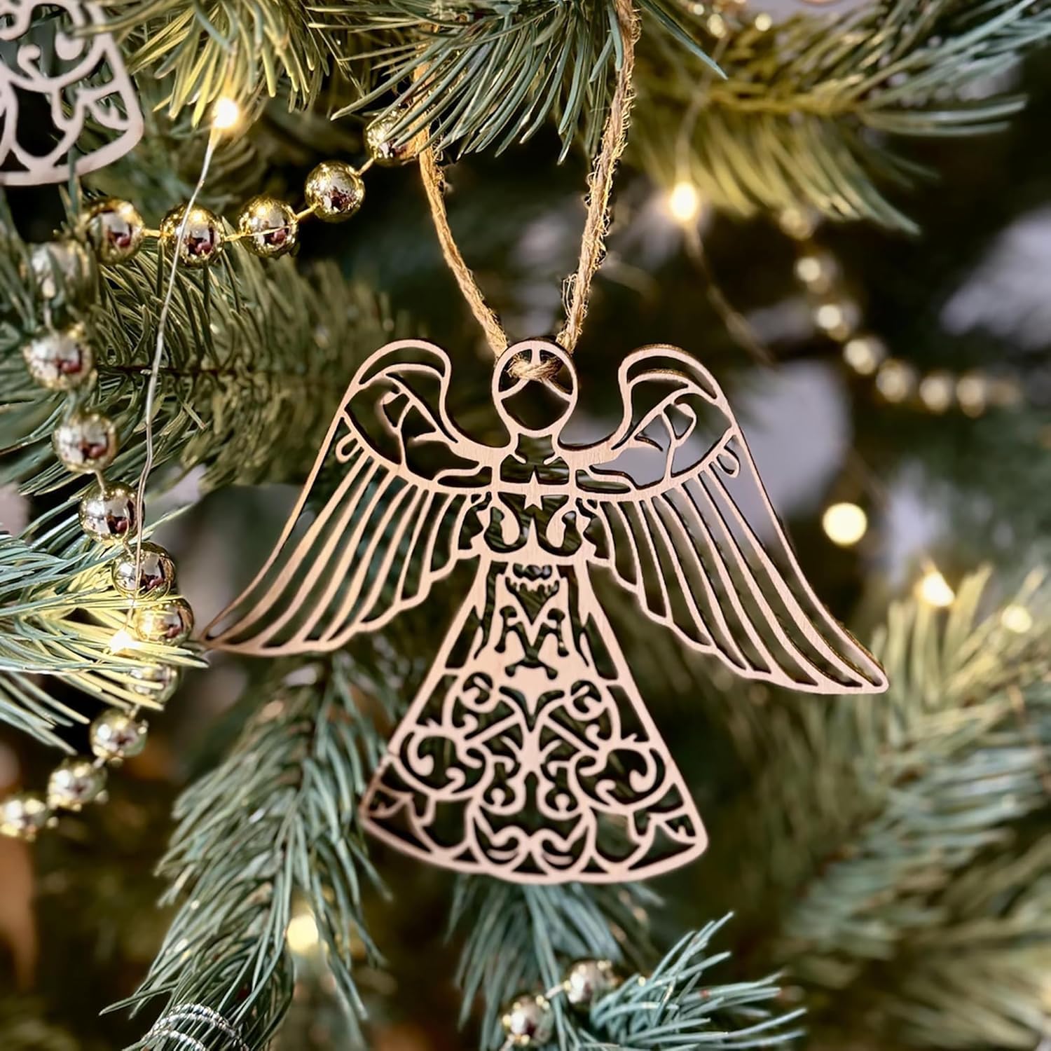 Decorative angel ornament hanging on a Christmas tree with lights.