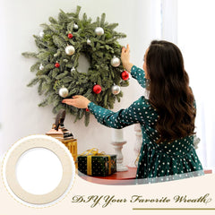 Woman decorating a Christmas wreath with ornaments on a white wall.
