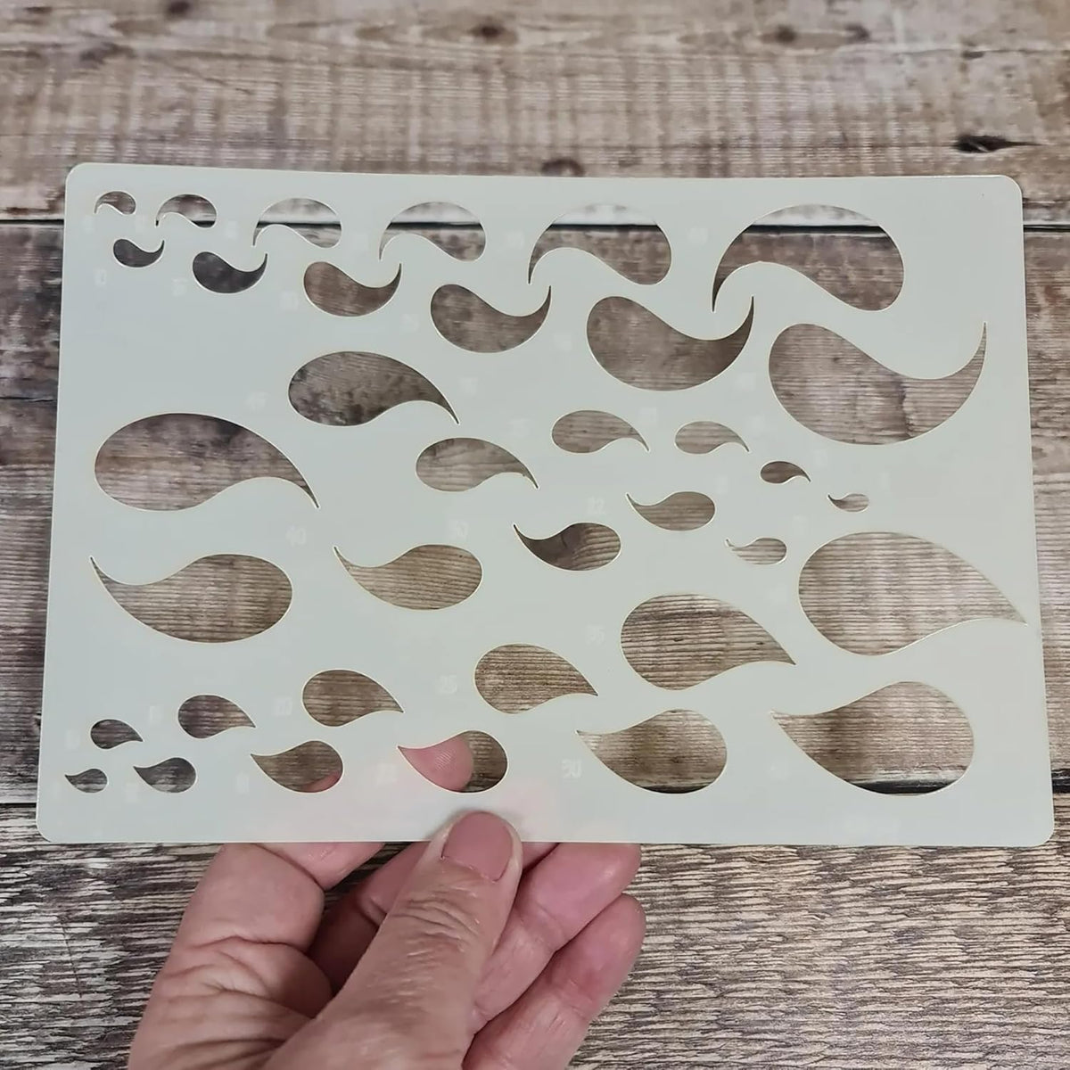 Stencil with wavy line pattern held by a hand on a wooden surface