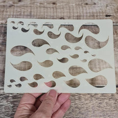 Stencil with wavy line pattern held by a hand on a wooden surface