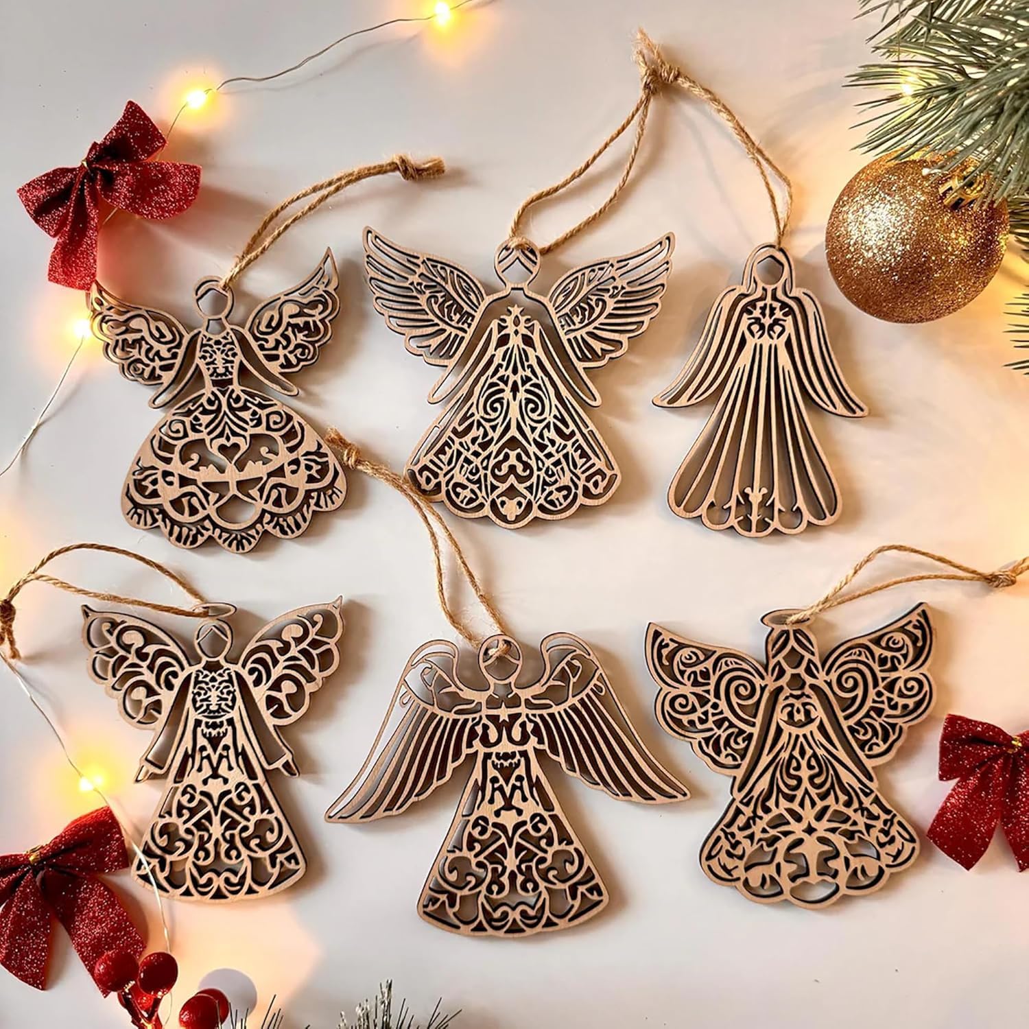 Decorative angel ornaments with intricate designs on a light background with string lights and red bows.