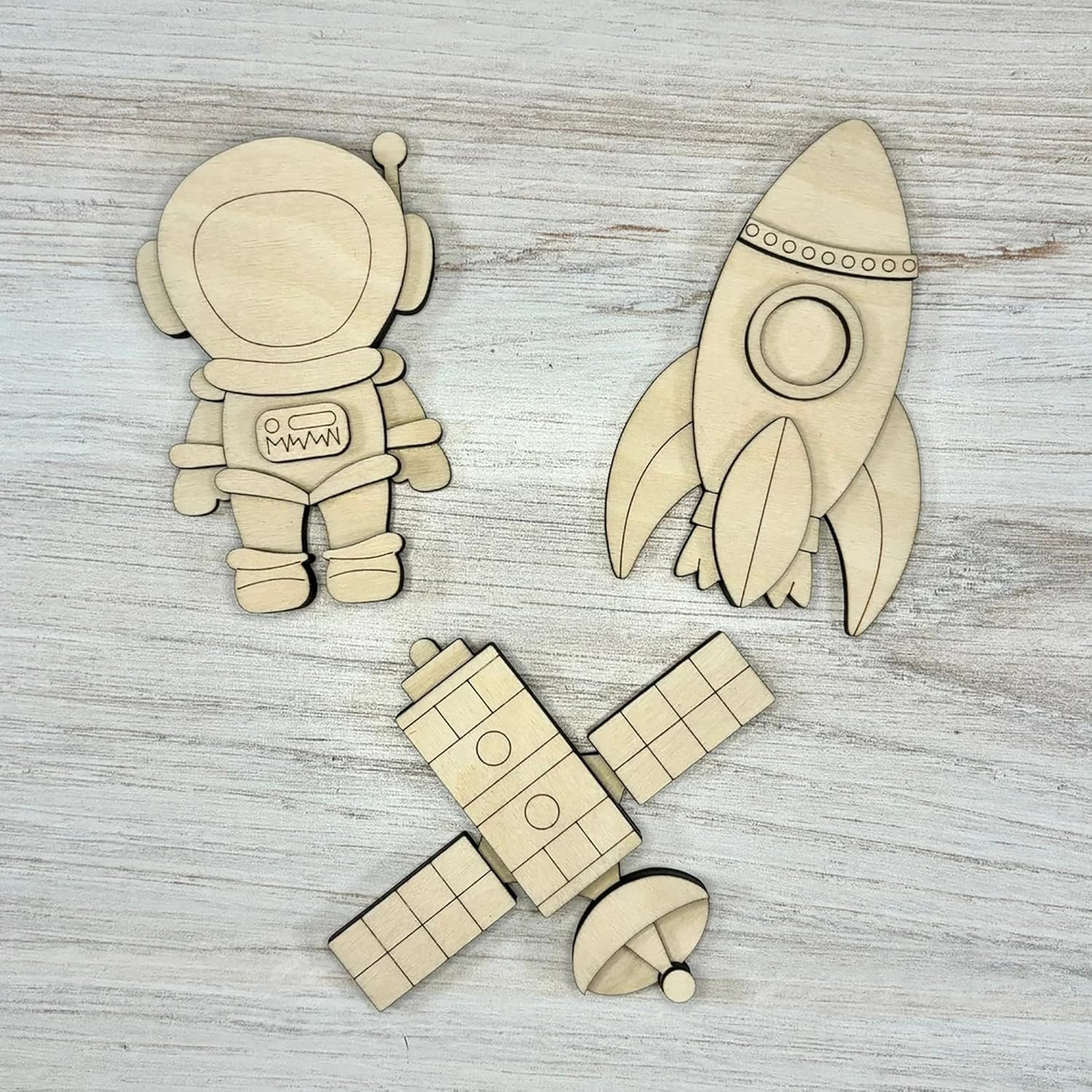 Wooden space-themed cutouts including an astronaut, rocket, and spaceship on a wooden surface.