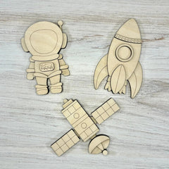 Wooden space-themed cutouts including an astronaut, rocket, and spaceship on a wooden surface.