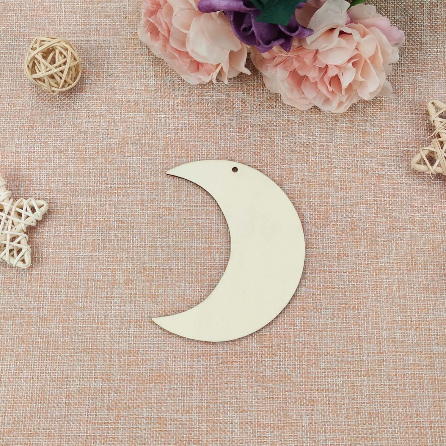 Wooden crescent moon ornament on a textured surface with flowers and decorative elements.