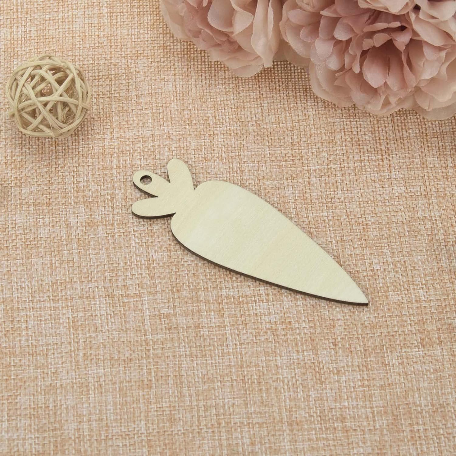 Decorative knife-shaped object on a textured beige surface with pink flowers and a decorative ball.