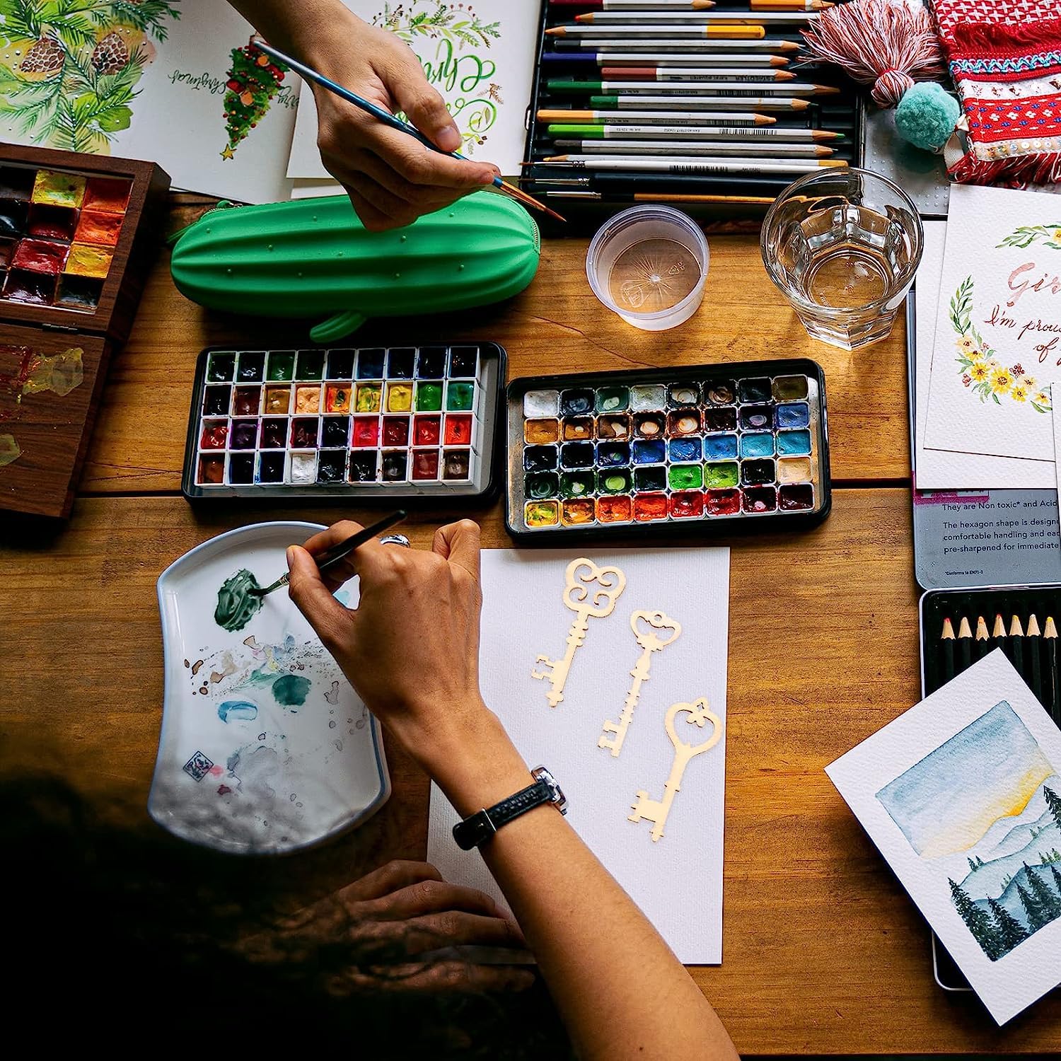 Artistic workspace with watercolor paints, brushes, and art supplies on a wooden table.