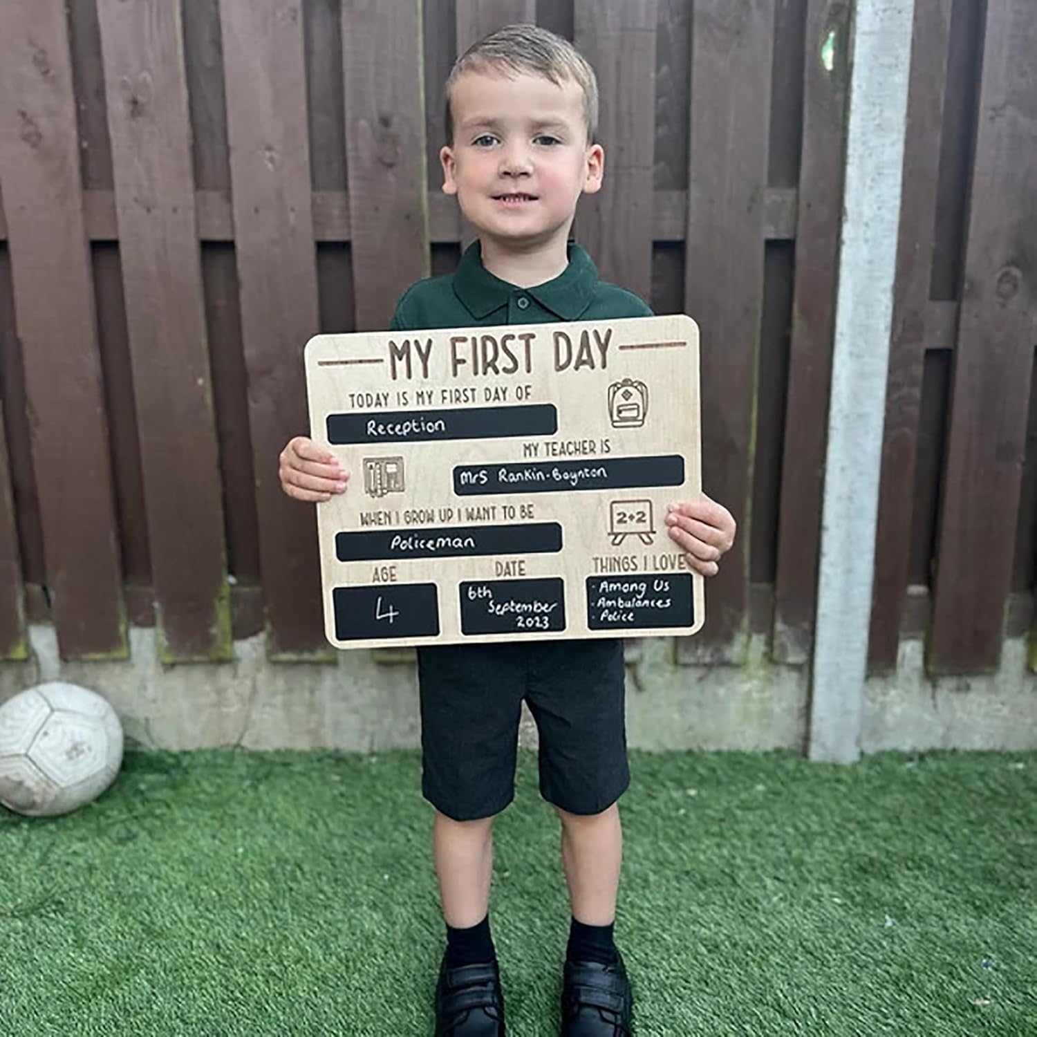 Young boy holding a sign for his first day of school in front of a wooden fence.
