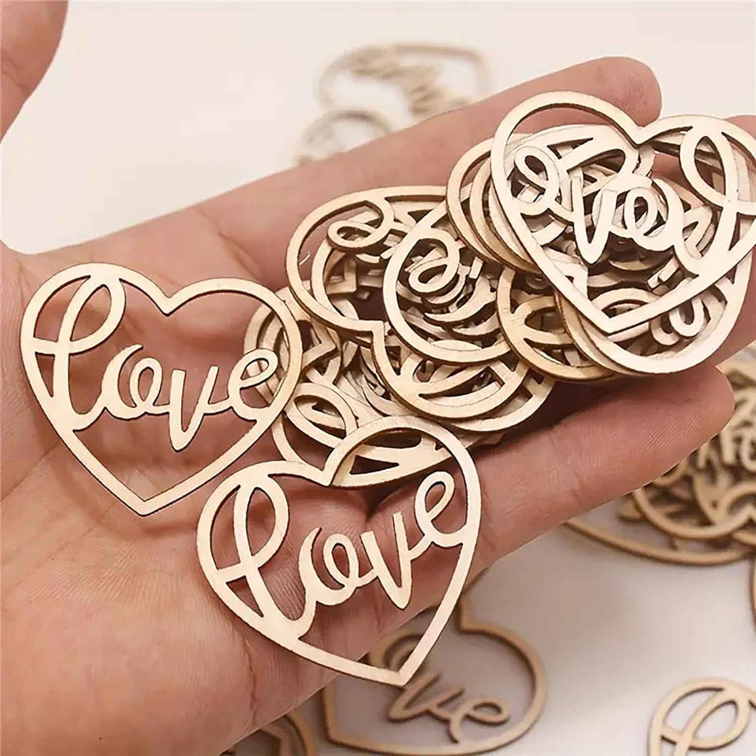 Hand holding wooden heart-shaped 'love' ornaments on a light background