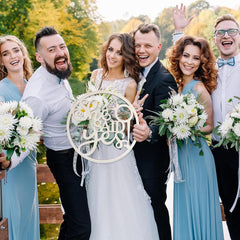 Wedding party holding a 'We Say I Do' sign outdoors with greenery in the background