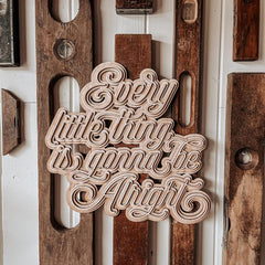 Wooden decorative sign with 'Every little thing is gonna be alright' text on a wooden background.
