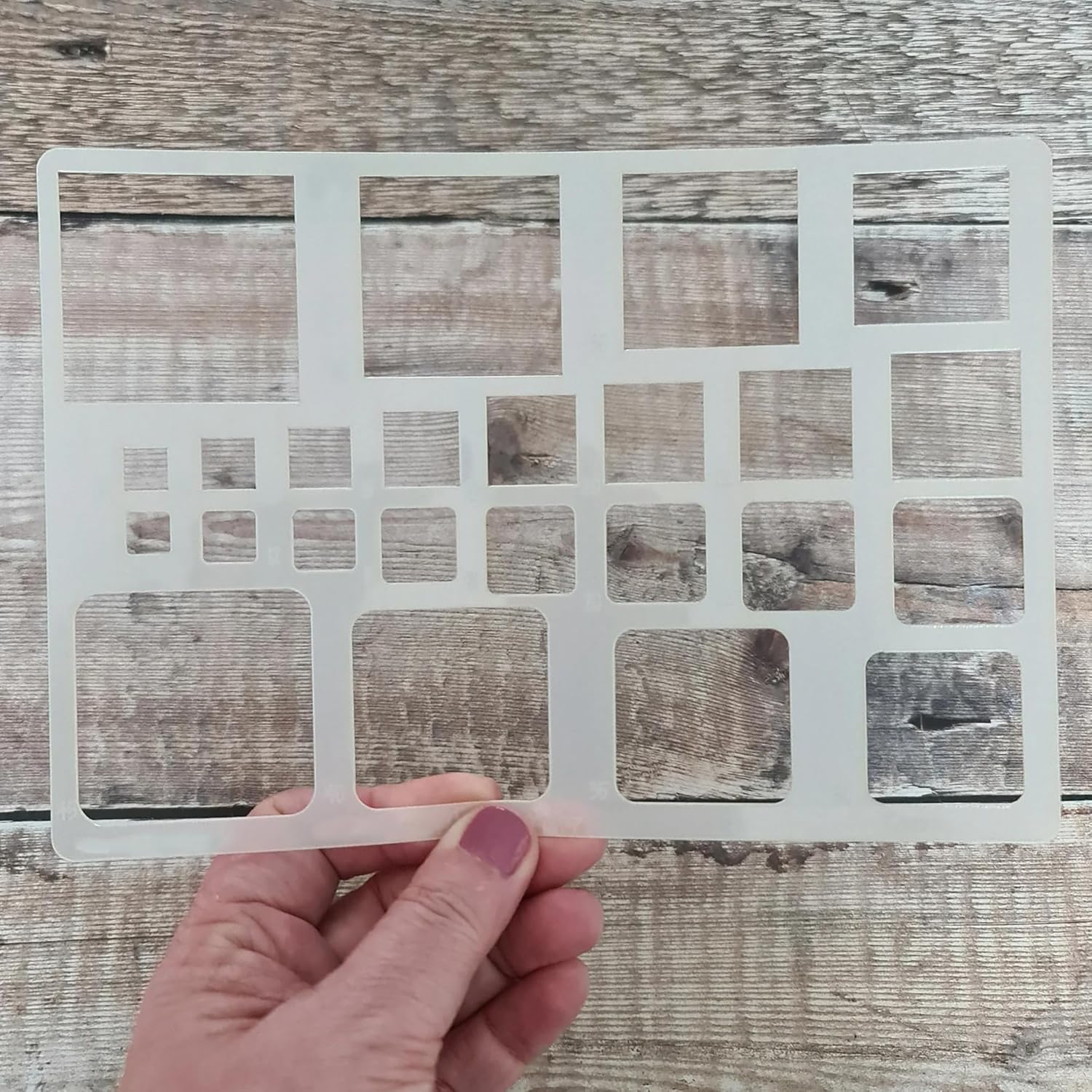 Hand holding a white plastic grid against a wooden background