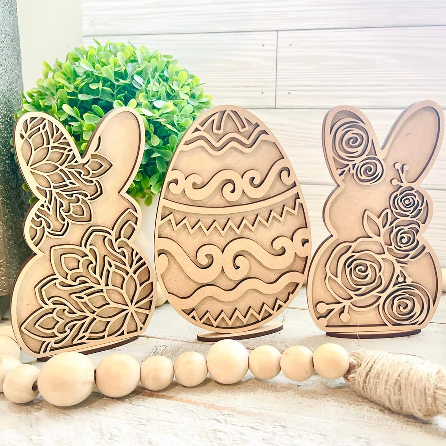 Three wooden Easter decorations shaped like a bunny, egg, and another bunny on a light wooden surface.
