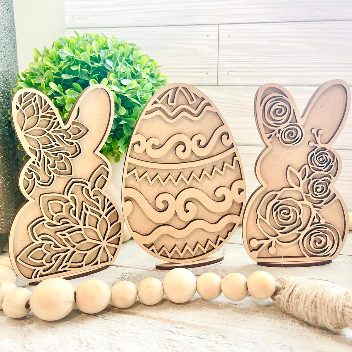 Three wooden Easter decorations shaped like a bunny, egg, and another bunny on a light wooden surface.