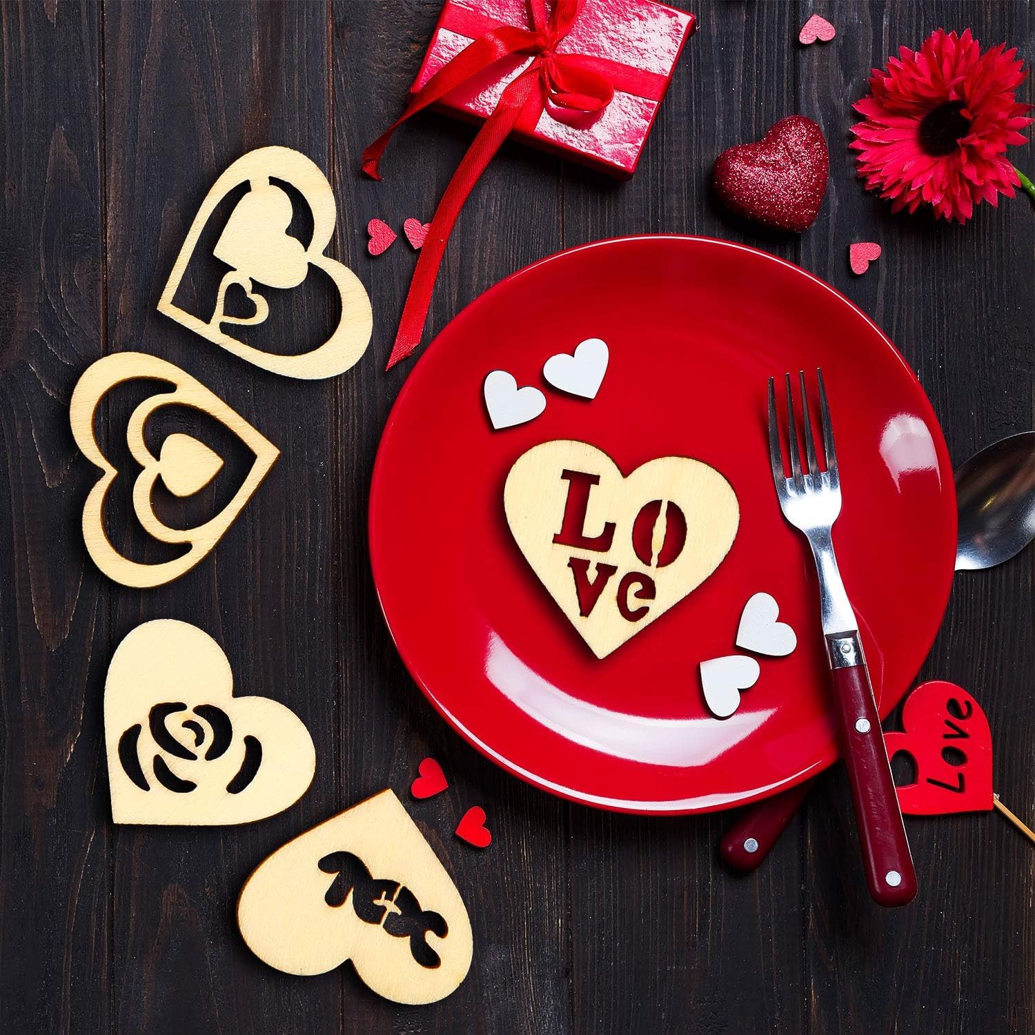 Red plate with heart-shaped 'LOVE' cutout, red gift box, and decorative flowers on a dark wooden surface.