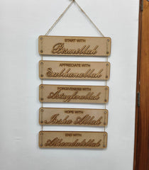Decorative wall hanging with engraved phrases on a white wall.