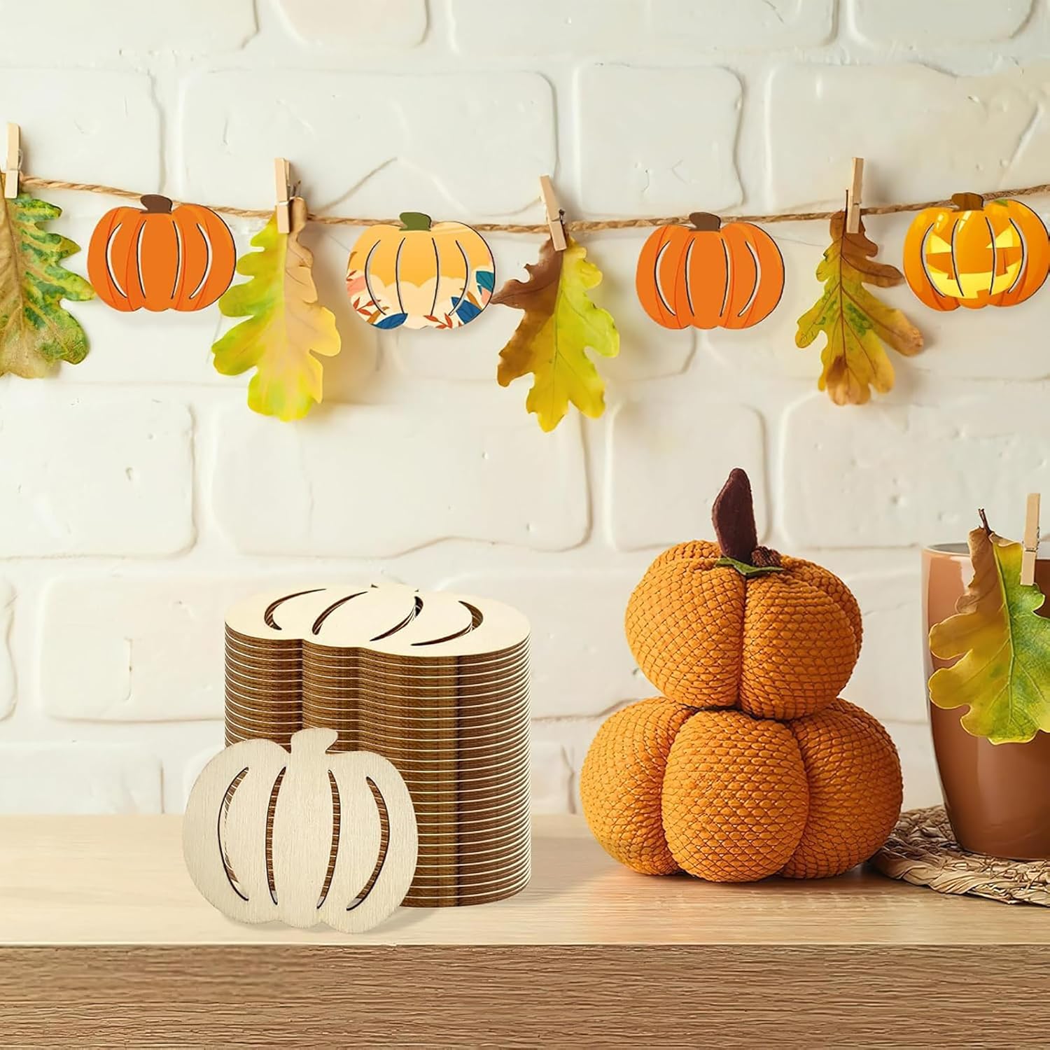 Decorative setup with pumpkins, leaves, and a stack of plates on a wooden surface against a white brick wall.