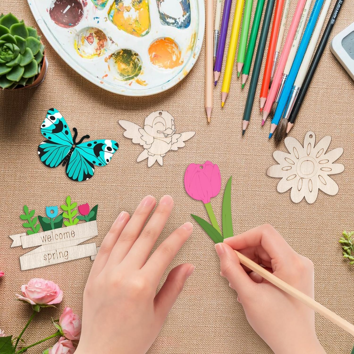 Hands working with paper cutouts of a butterfly, flower, and fairy on a textured surface with art supplies.