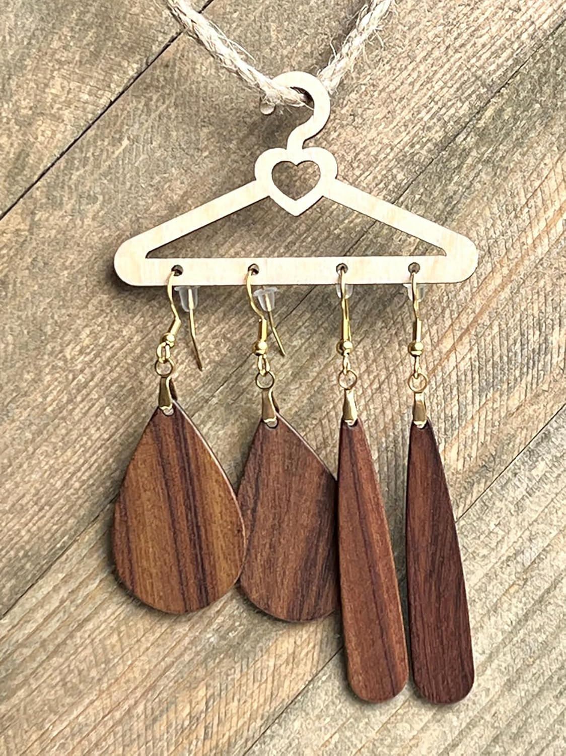 Wooden teardrop earrings hanging on a heart-shaped hanger against a wooden background
