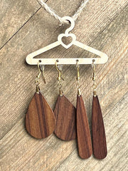 Wooden teardrop earrings hanging on a heart-shaped hanger against a wooden background