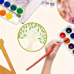 Artistic setup with watercolor paints, a palette, and a hand holding a brush near a painted tree design.