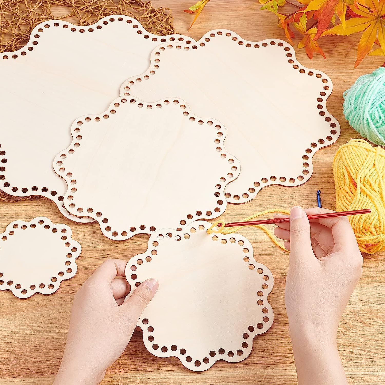 Hands working with crochet hooks and yarn on a wooden surface with decorative cut-out paper.