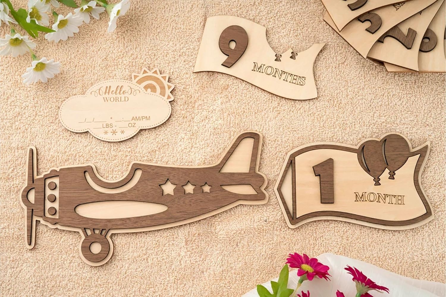 Wooden baby milestone markers including an airplane, number '9' with a crown, and '1' with balloons on a textured surface.