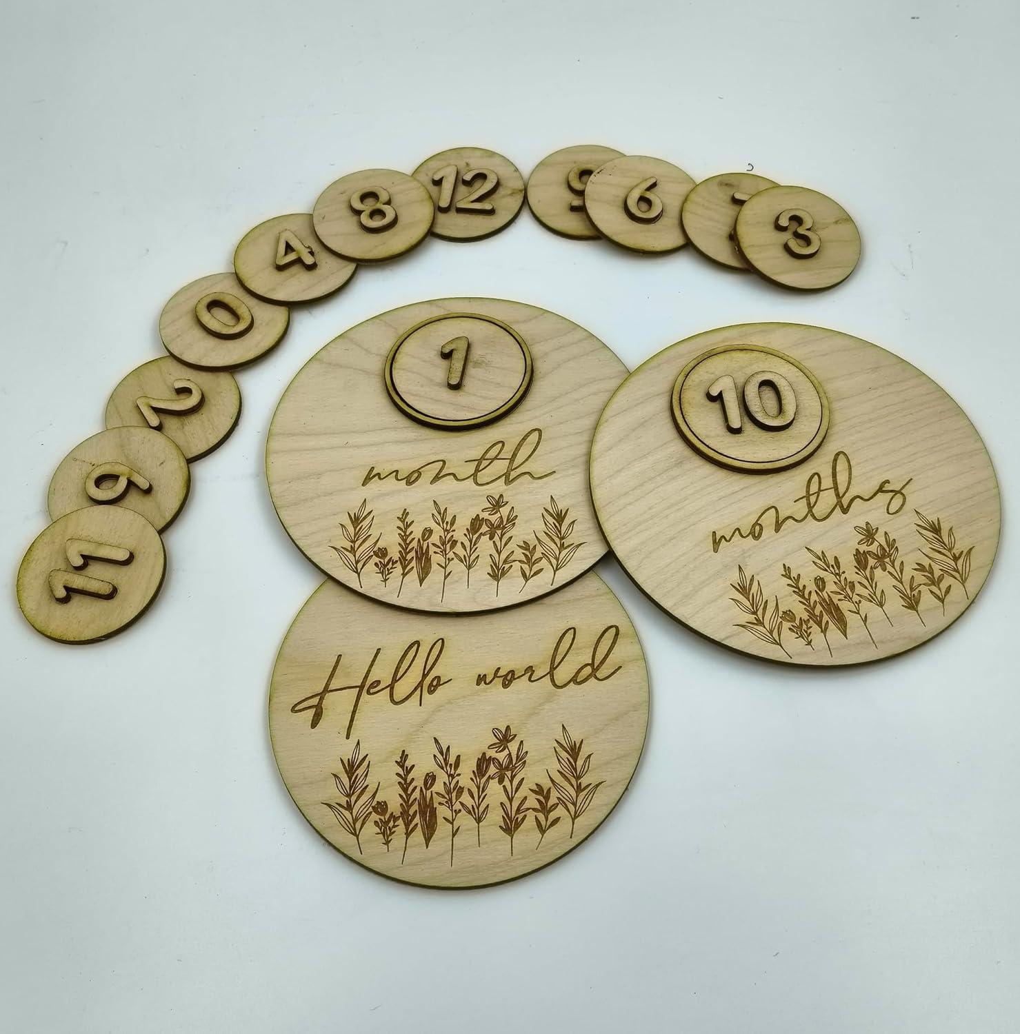 Wooden baby milestone discs with numbers and engraved text on a white background