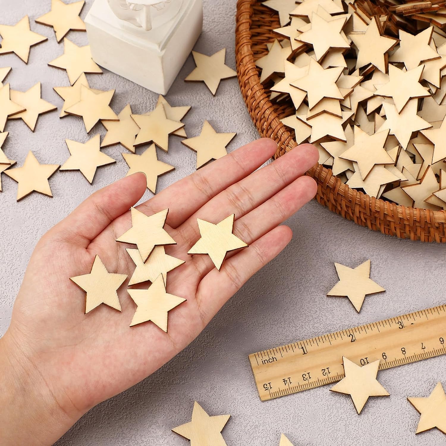 Hand holding wooden stars with a basket and ruler on a gray surface