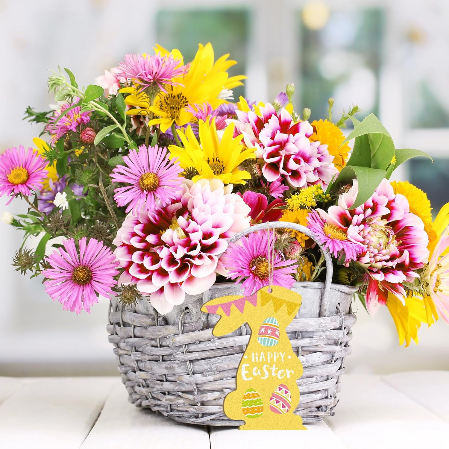 Bouquet of flowers in a basket with a 'Happy Easter' sign on a white surface.