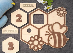 Wooden baby milestone cards with bee and flower designs on a textured surface.