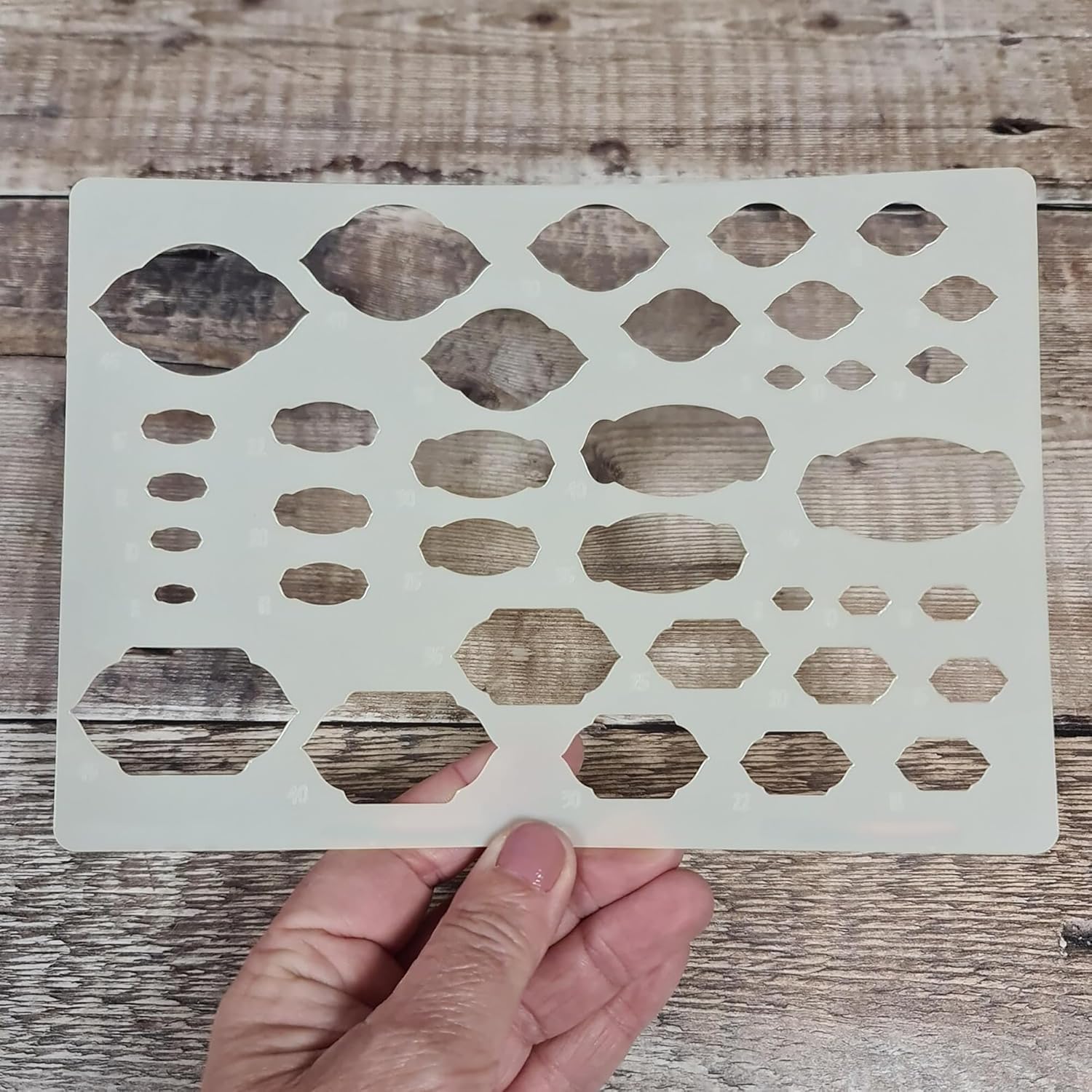 Hand holding a stenciling template with geometric shapes on a wooden surface