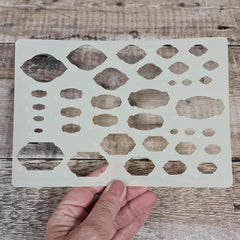 Hand holding a stenciling template with geometric shapes on a wooden surface