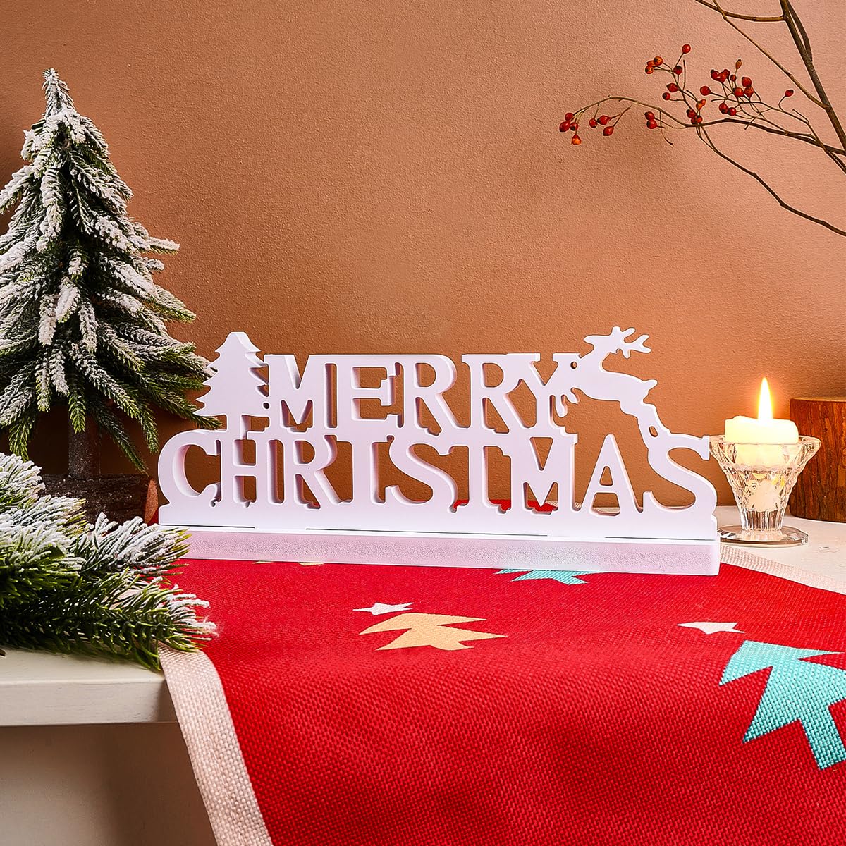 Decorative 'Merry Christmas' sign with a candle and Christmas tree on a red tablecloth.