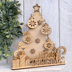 Wooden Christmas tree decoration with 'Merry Christmas' text on a light wooden background.