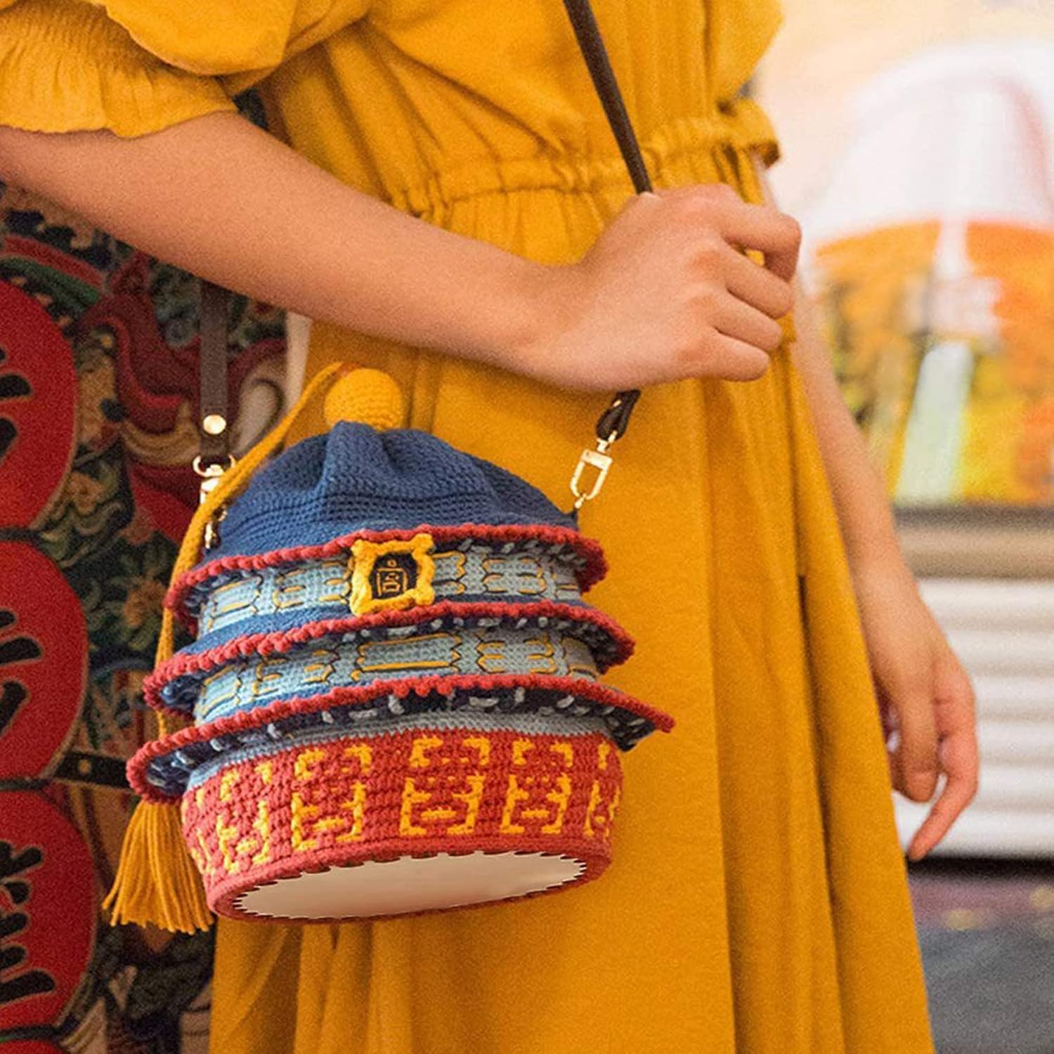 Person holding a colorful woven bag with intricate patterns, wearing a yellow dress.