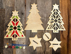 Wooden Christmas tree and star decorations on a wooden surface with paint supplies.