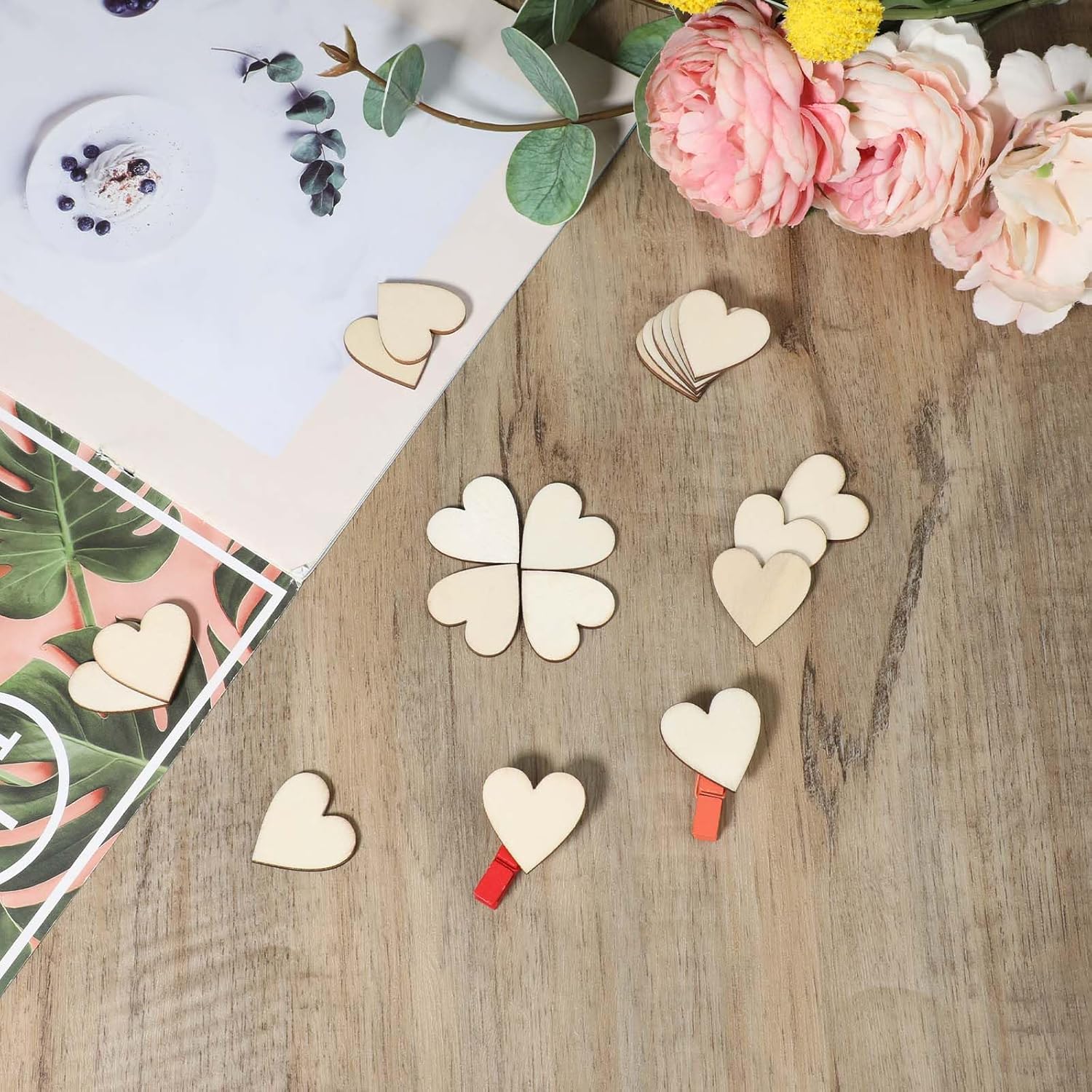 Wooden heart-shaped clips on a wooden surface with flowers and a magazine.