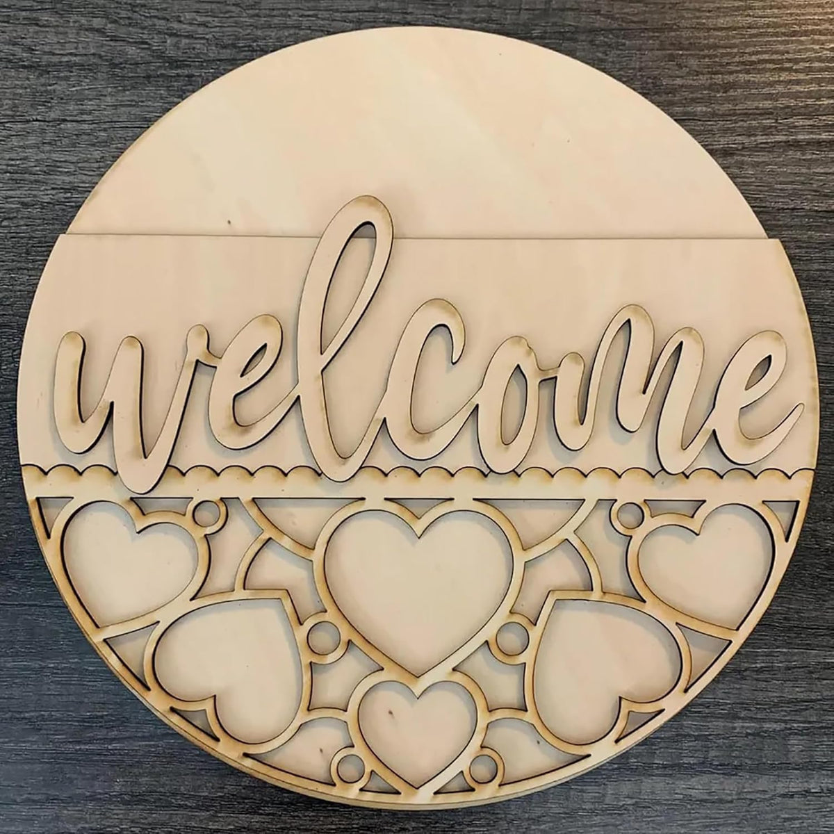 Round wooden decorative piece with 'welcome' text and heart shapes on a dark surface
