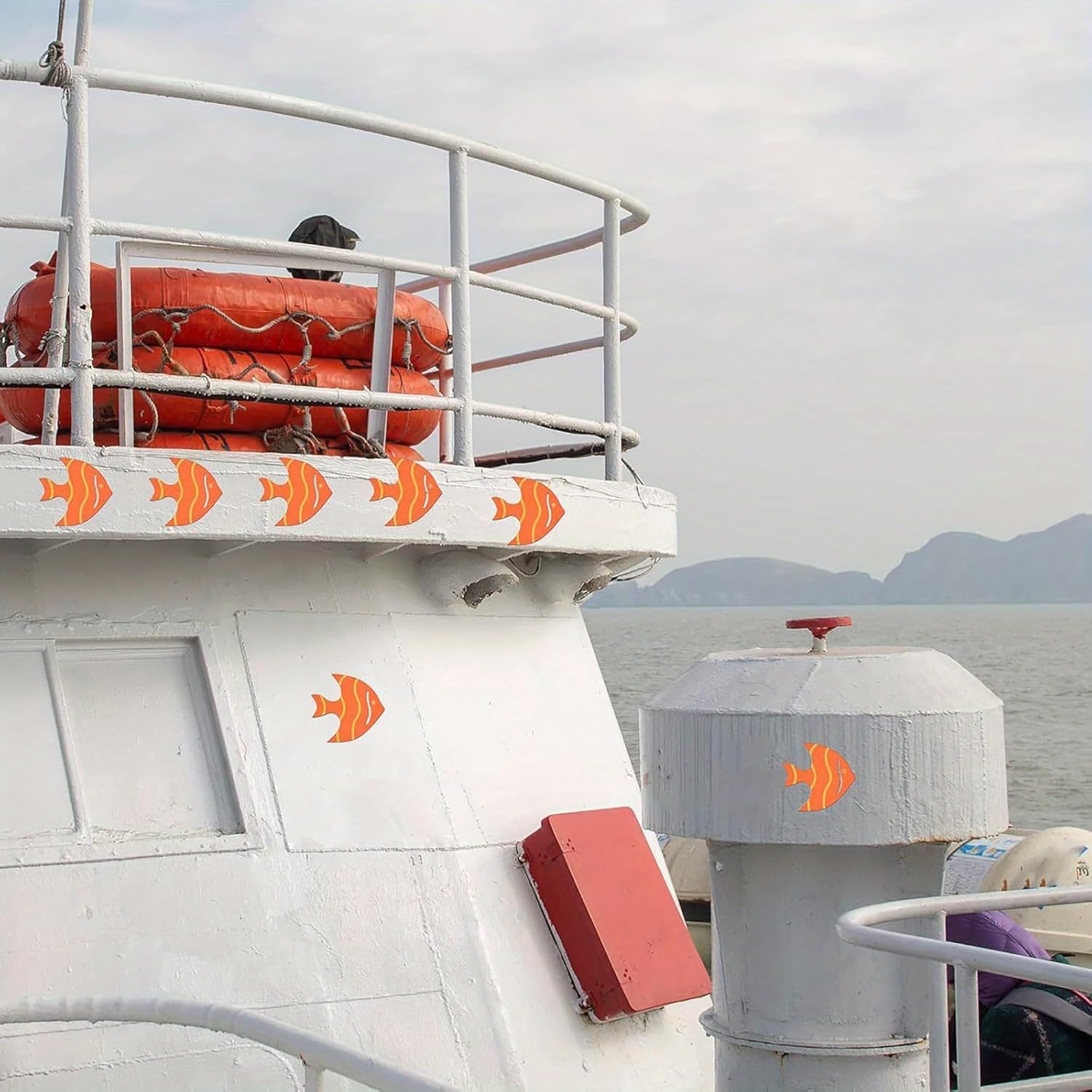 Close-up of a boat with life buoys and orange fish decals on a cloudy day.