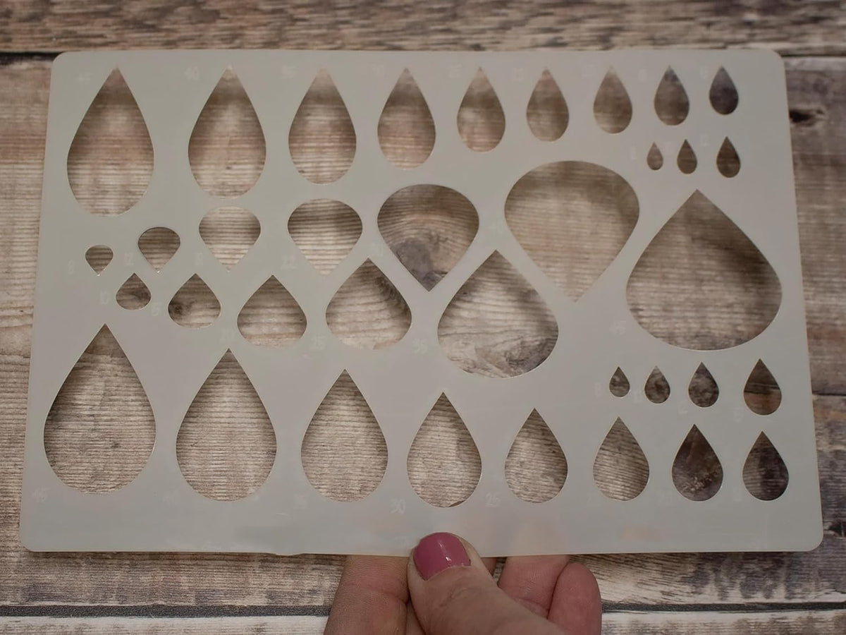 Wooden stencils with teardrop shapes held by a hand on a wooden surface