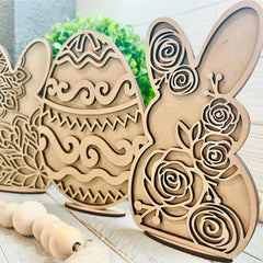 Wooden Easter decorations including a bunny and eggs with floral patterns on a light wooden surface.